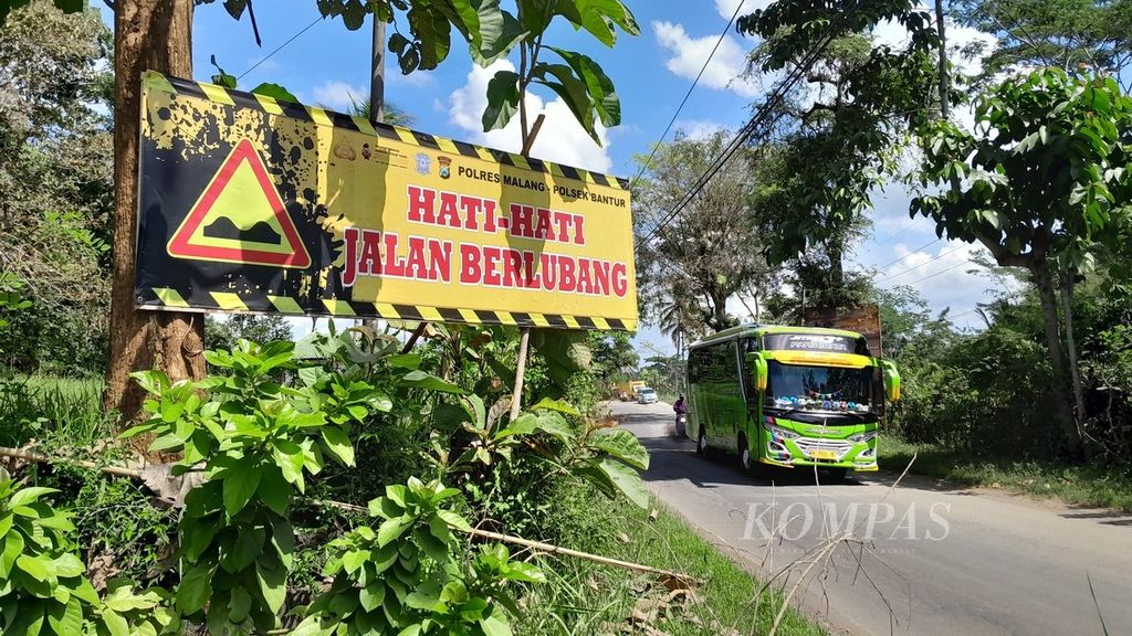 Sebuah bus wisata melaju keluar dari titik jalanan rusak di Kecamatan Bantur, Kabupaten Malang, Jawa Timur, Minggu (16/7/2023). Tampak sebuah papan pemberitahuan kondisi jalan rusak bagi pengendara dari arah berlawanan.