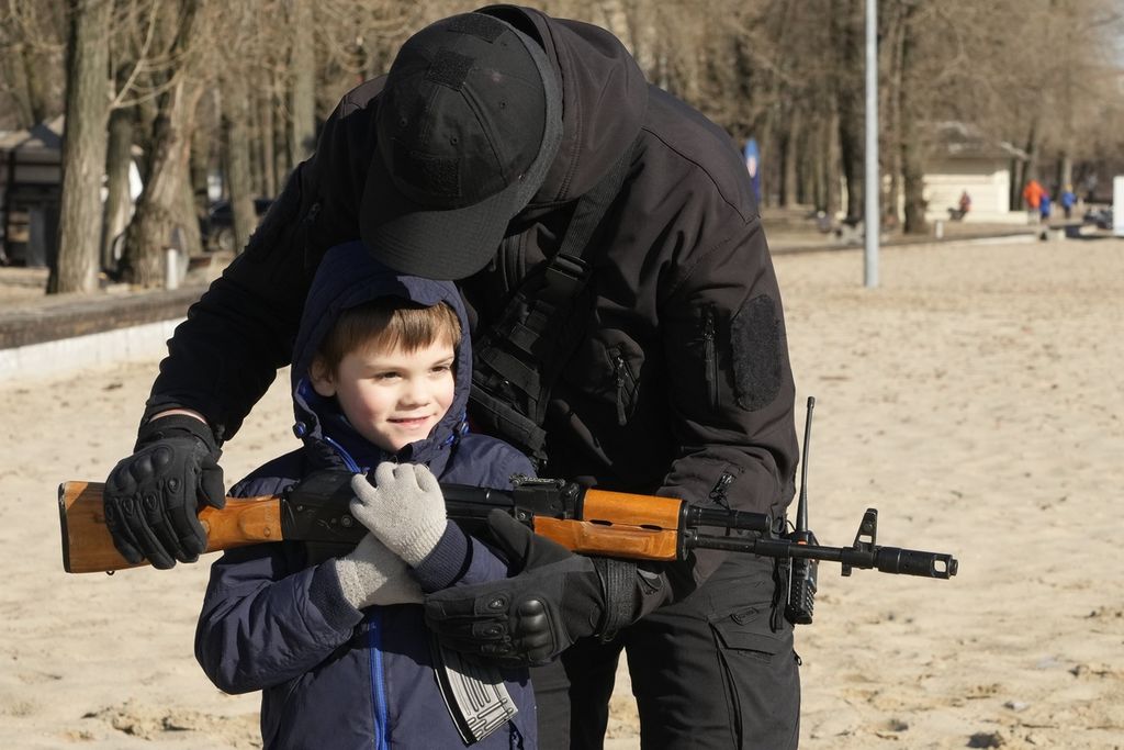 Seorang anggota kelompok sayap kanan Ukraina membantu seorang anak laki-laki untuk memegang senapan serbu Kalashnikov selama pelatihan di Kyiv, Ukraina, Minggu (13/2/2022). 