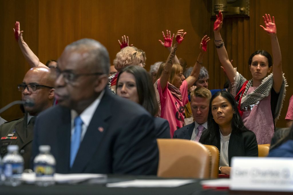 Dozens of demonstrators hold up their palms that have been painted with red paint, symbolizing civilian casualties in Palestine, as United States Defense Secretary Lloyd Austin and Chief of Staff of the US Air Force General CQ Brown provide a statement during a Senate hearing at the Capitol Building in Washington DC, USA, on Wednesday (8/5/2024).