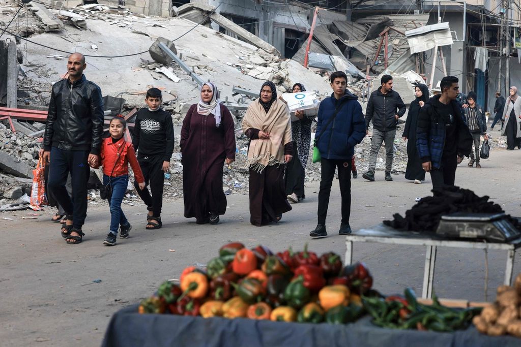 Warga Palestina berjalan melewati bangunan yang hancur di Rafah di selatan Jalur Gaza, Minggu (14/1/2024). 