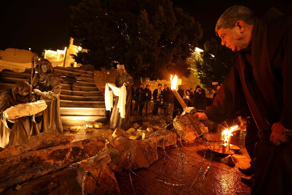 Seorang imam menyalakan lilin pada instalasi kandang Natal di depan Gereja Kelahiran (Nativity Church), Bethlehem, wilayah pendudukan Tepi Barat, dengan sosok yang diumpamakan bayi Yesus berbaring di palungan di tengah puing-puing, merujuk pada kondisi di Gaza, Sabtu (23/12/2023). 