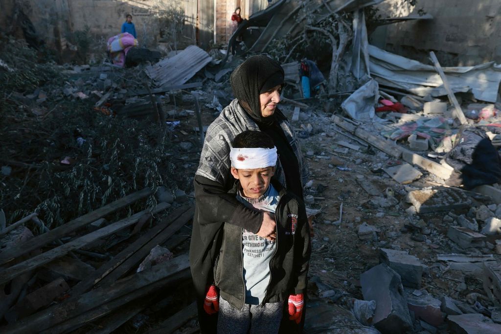 Seorang perempuan warga Palestina memeluk seorang anak yang terluka ringan saat mereka memeriksa reruntuhan bangunan menyusul serangan bom Israel di Rafah, Jalur Gaza selatan, Kamis (18/1/2024). 