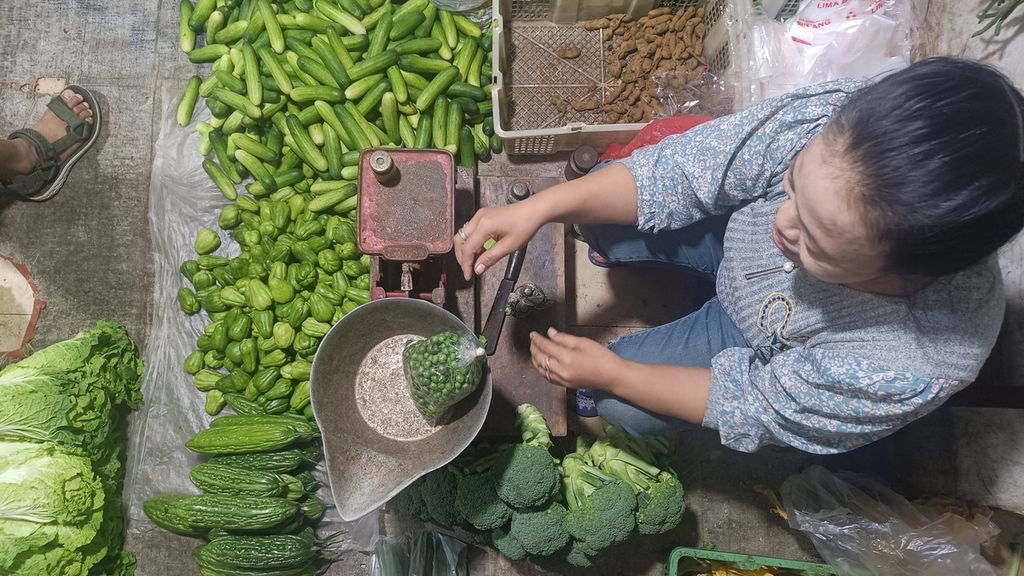 Suparni (53), pedagang di lokasi binaan Pasar Pisang, Jakarta, saat menimbang sayuran yang dijualnya, Senin (13/2/2023). Mayoritas dagangannya berupa sayuran, seperti kacang panjang, brokoli, terong, timun, labu, jengkol, dan sawi.