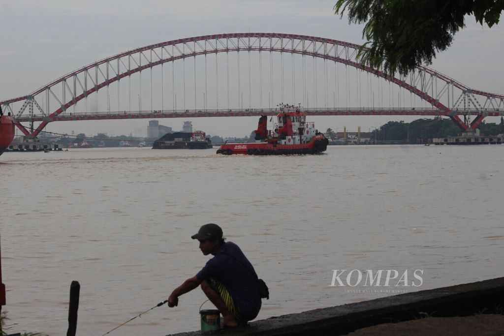 Warga memancing di tepian Sungai Musi dengan berlatarkan Jembatan Musi VI, Palembang, Jumat (15/1/2021).