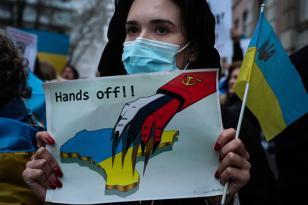 Seorang demonstran memegang tanda yang menggambarkan Ukraina dan bertuliskan <i>Hands off!</i> dalam aksi protes terhadap operasi militer Rusia di Ukraina, Kamis (24/2/2022), di depan Kedutaan Besar Rusia di Lisabon, Portugal. Pemerintah Ukraina mengumumkan sebanyak 57 orang tewas dan 169 orang lainnya luka-luka.