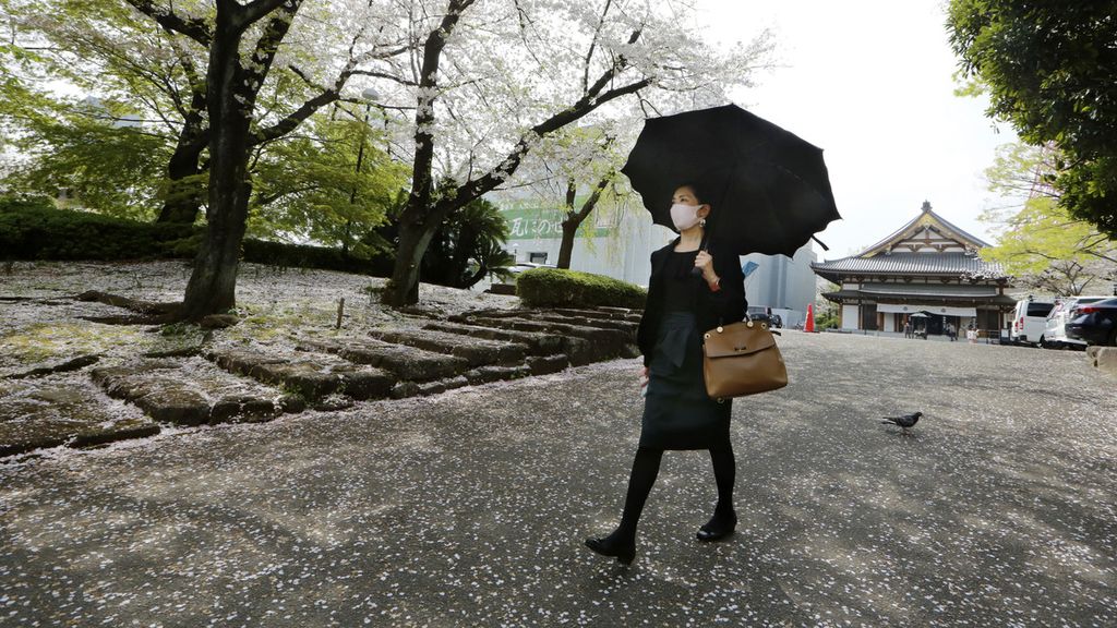 Perempuan berjalan di bawah pohon sakura yang sedang mekar di Tokyo, Jepang, Selasa (30/3/2021). (AP/Koji Sasahara)