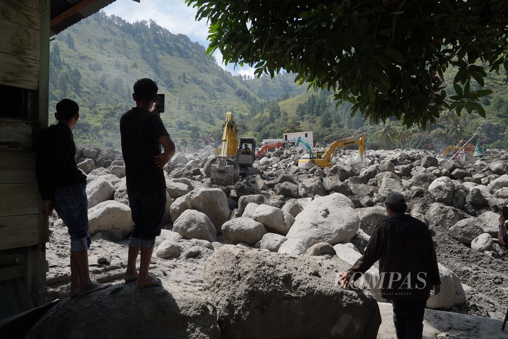 Warga menyaksikan alat berat yang digunakan untuk menyingkirkan batuan besar yang berserakan akibat banjir bandang di Desa Simangulampe, Kecamatan Baktiraja, Kabupaten Humbang Hasundutan, Sumatera Utara, Selasa (5/12/2023). 