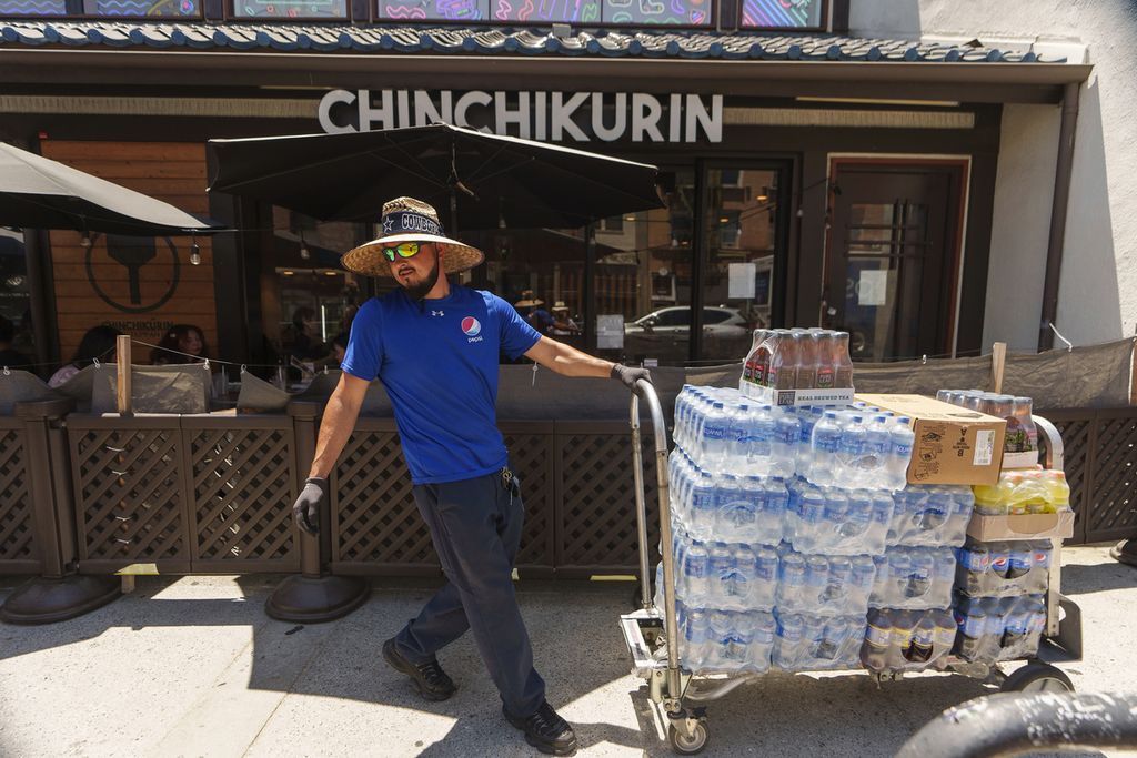 Seorang pengemudi bernama Jose Viveros mengirimkan pesanan makanan dan minuman untuk pelanggan di Distrik Little Tokyo, Los Angeles pada Kamis (27/7/2023).