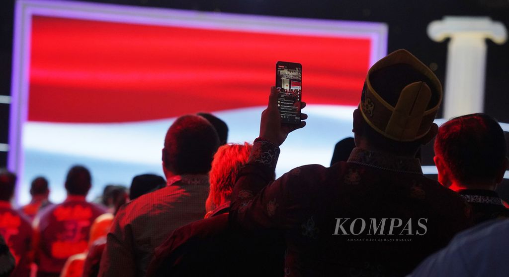 Seorang hadirin melakukan siaran langsung di media sosialnya ketika menyanyikan lagu Indonesia Raya pada pembukaan Debat Putaran ke-5 Calon Presiden Pemilu 2024 di Jakarta Convention Center, Jakarta, Minggu (4/2/2023).