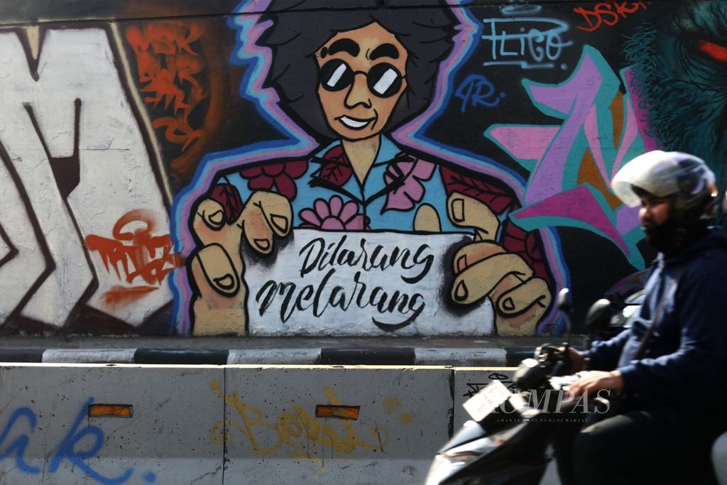 A motorcyclist crosses a mural containing the words "dilarang melarang (forbidden forbid)" on the flyover wall in Grogol, Jakarta, Friday (11/15/2019). This mural is a satire against the Criminal Code Bill which is considered too regulated the private affairs of citizens.