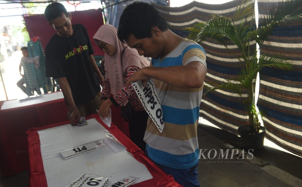 Petugas menyiapkan label panitia saat pembuatan Tempat Pemungutan Suara (TPS) 08 di Kranggan Margorejo, Wonocolo, Surabaya, Selasa (13/2/2024). Keterbatasan tempat membuat TPS dibangun di atas trotoar di pinggir Jalan Frontage Ahmad Yani. Anggota KPPS yang membangun TPS harus ekstrakreatif memanfaatkan ruang yang terbatas, juga menambah bahan agar TPS tahan saat hujan. 