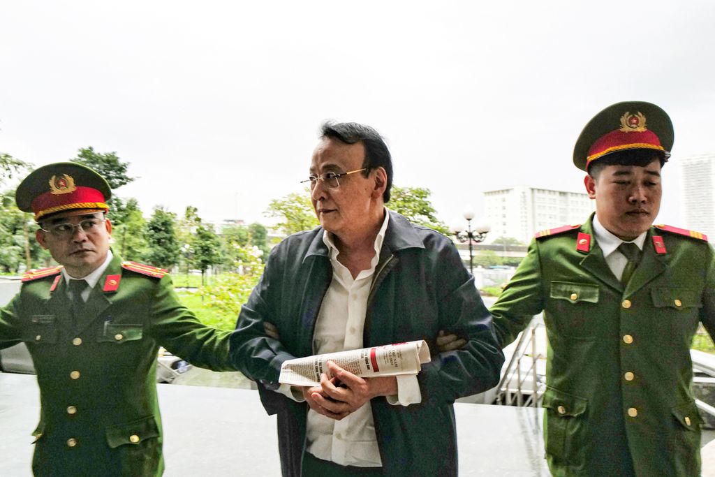 Dua polisi mengawal pemimpin grup bisnis Tan Hoang Minh, Do Anh Dung (tengah), menuju ruang sidang di Hanor, 19 Maret 2024. 