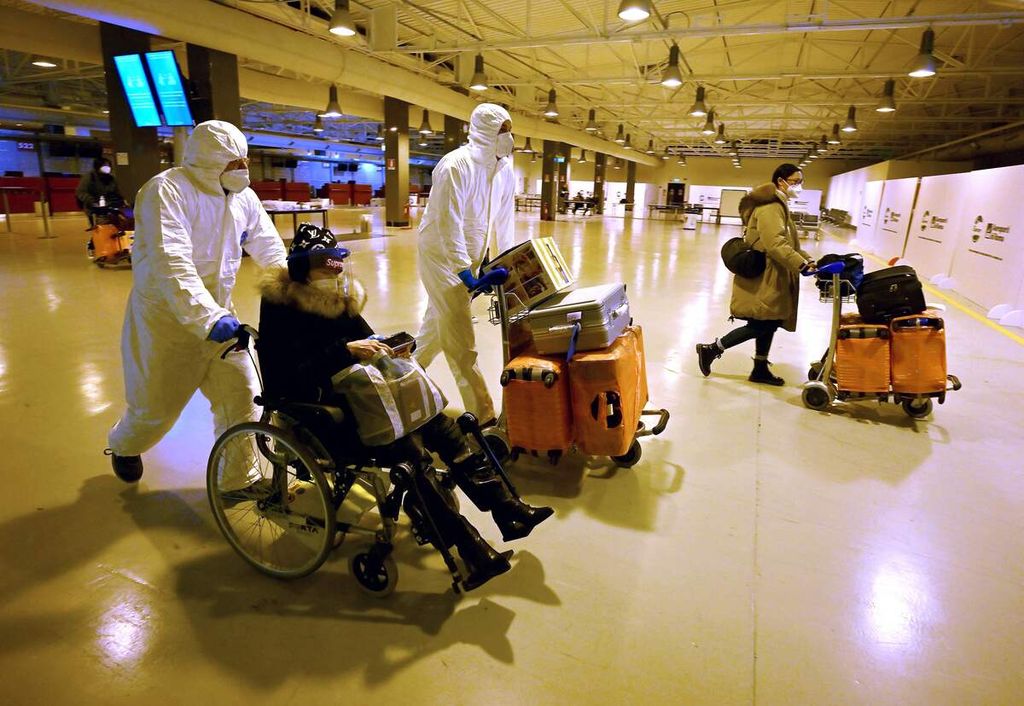 Sejumlah pekerja yang mengenakan alat pelindung diri dan masker membantu pelaju perjalanan dari China meninggalkan terminal kedatangan Bandara Internasional Fiumicino, dekat Roma, Italia, 29 Deesmber 2022, setelah menjalani pemeriksaan Covid-19. 