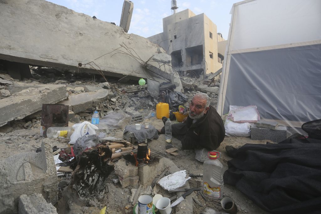 Seorang laki-laki warga Palestina menghangatkan diri di sebuah lokasi di tengah-tengah bangunan di Gaza yang runtuh karena serangan Israel, 27 Desember 2023. 