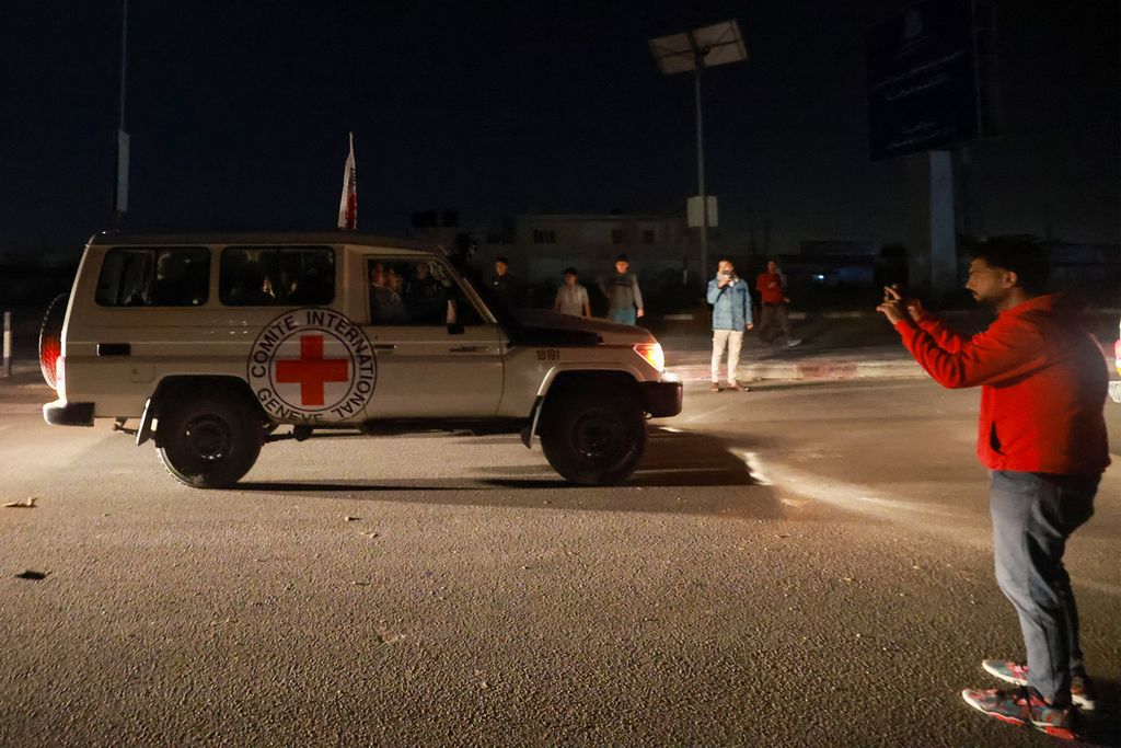 Seorang warga memotret kendaraan Palang Merah Internasional yang dilaporkan membawa sandera yang dibebaskan Hamas saat mereka melintasi titik perbatasan Rafah di Jalur Gaza menuju Mesir pada Jumat (24/11/2023). 