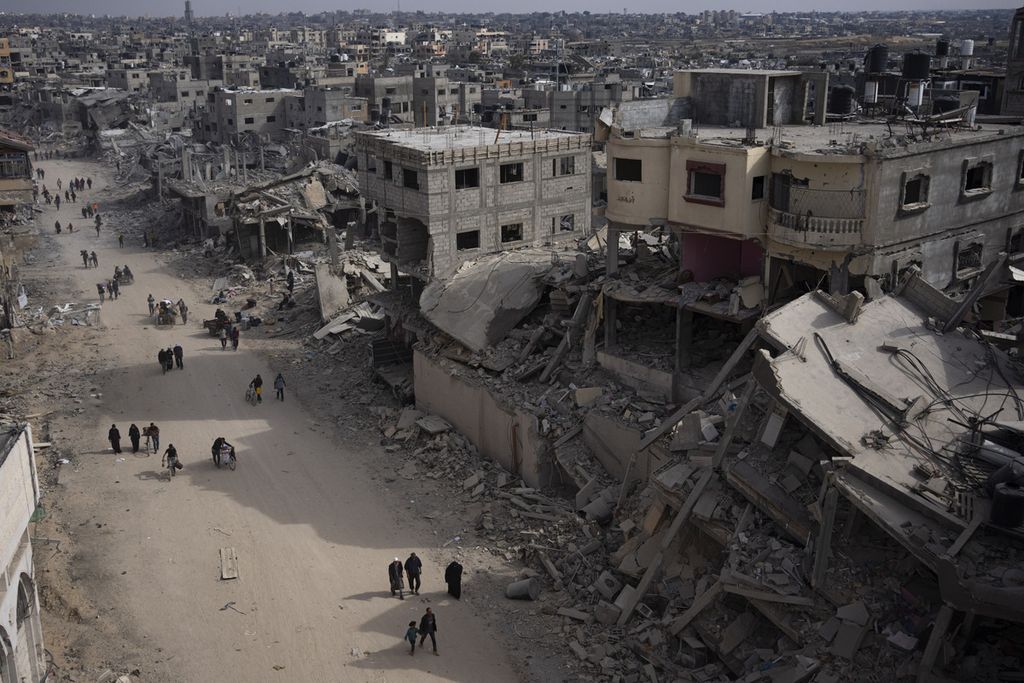 Warga Palestina berjalan di tengah reruntuhan bangunan di Khan Younis, kota di Gaza selatan, Senin (8/4/2024).
