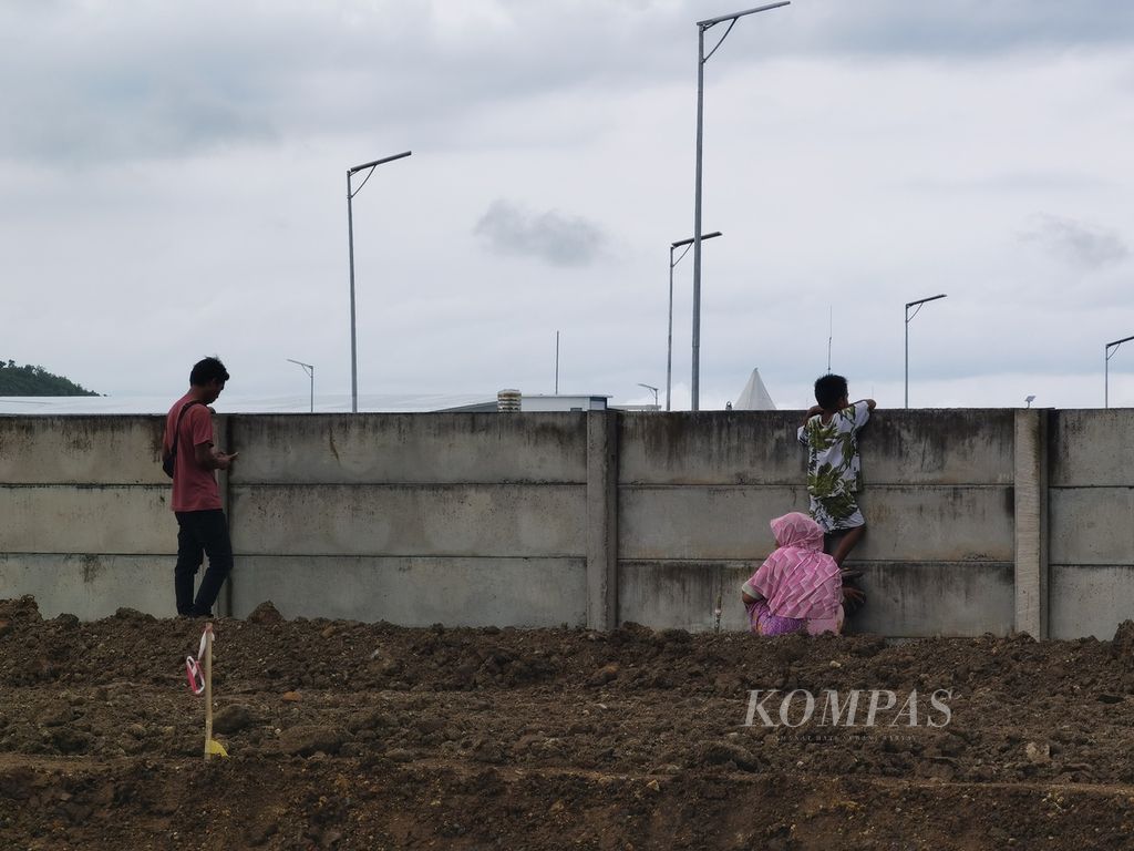 Seorang ibu membantu anaknya untuk memanjat pagar demi bisa melihat jalannya tes pramusim MotoGP di Sirkuit Internasional Jalan Raya Pertamina Mandalika, Kuta, Pujut, Lombok Tengah, Nusa Tenggara Barat, Jumat (11/2/2022).