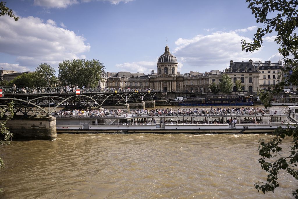 Perahu turis melintas di bawah jembatan Pont des Arts di Sungai Seine, Paris, Perancis, Senin (24/6/2024). Suhu udara pada musim panas tahun ini lebih tinggi akibat perubahan iklim. 