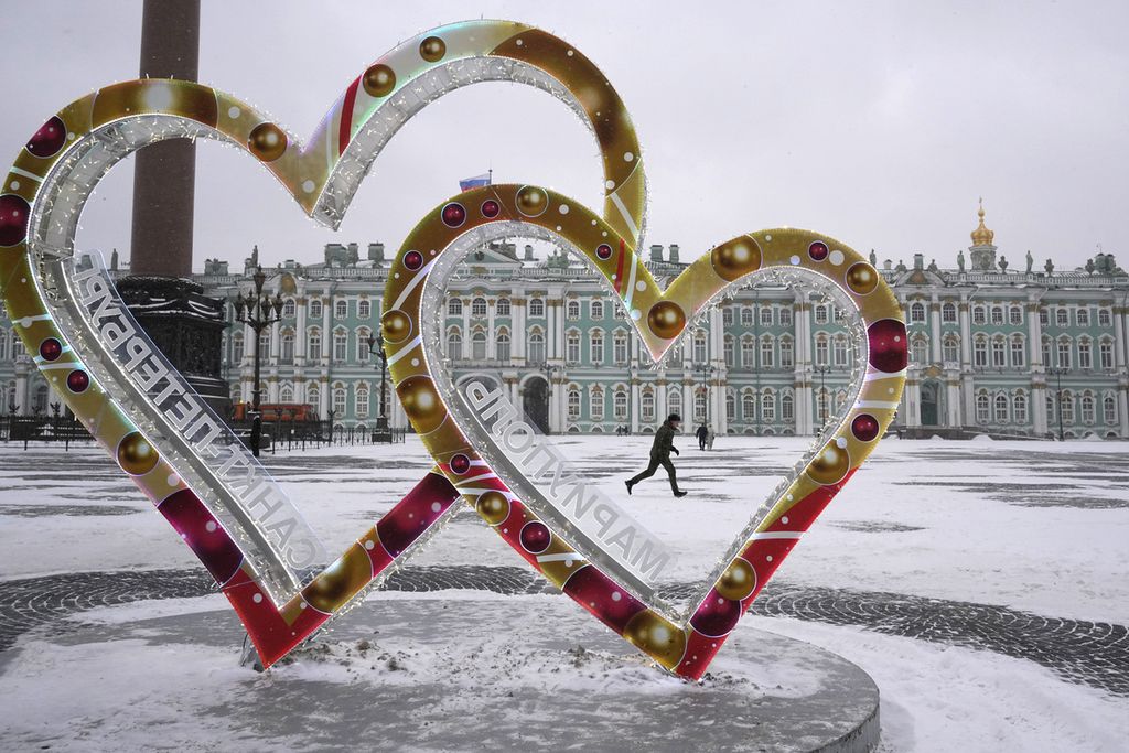 Seorang anggota militer Rusia melewati dua ornamen berbentuk hati melambangkan cinta yang terpasang di Palace Square, St Petersburg, Rusia, Senin (12/12/2022). 