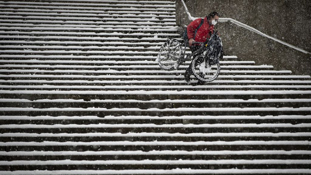 Warga dengan masker mengangkat sepeda saat menuruni tangga kampus yang dipenuhi salju di Universitas Simon Fraser, Burnaby, British Columbia, Kanada, Senin (21/12/2020). 