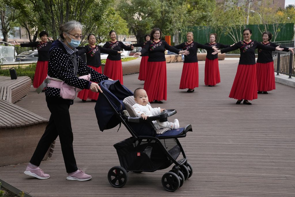Seorang perempuan mendorong kereta bayi melintasi para penari di sebuah taman di Beijing, China, 14 Oktober 2021.  