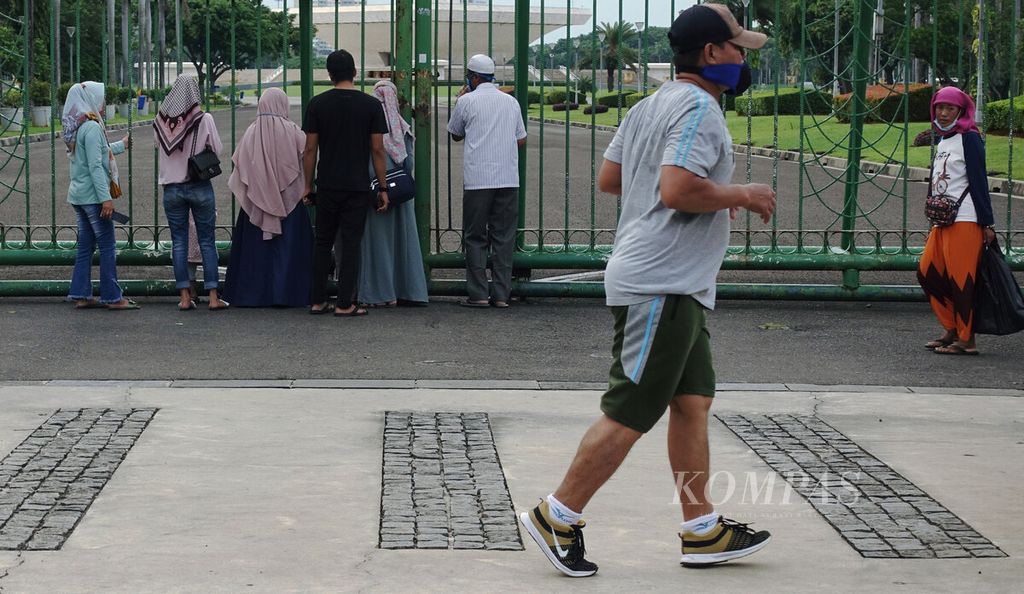 Residents enjoy the atmosphere of Monas from behind a fence in Gambir, Central Jakarta, Thursday (10/2/2022). The cases of the Omicron variant of Covid-19 are increasing and surpassing the wave of cases of the Delta variant.