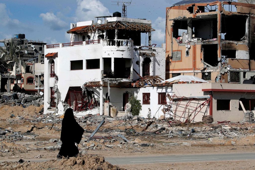 Seorang perempuan berjalan di depan bangunan yang hancur akibat serangan Israel di kamp Maghazi, Gaza, 1 Februari 2024. 