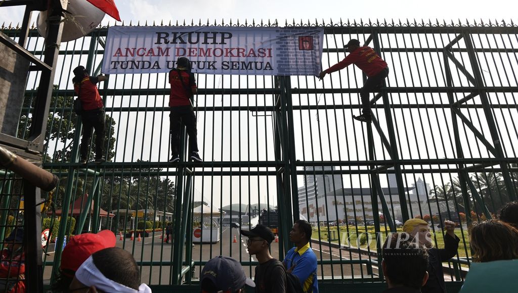 Peserta aksi memasang spanduk di pintu masuk Gedung DPR, Senayan, Jakarta, dalam unjuk rasa menolak Rancangan Kitab Undang-undang Hukum Pidana (RKUHP), Senin (16/9/2019). Aksi tersebut menyerukan penundaan RKUHP karena berpotensi mengancama kebebasan berpendapat bagi masyarakat sipil.