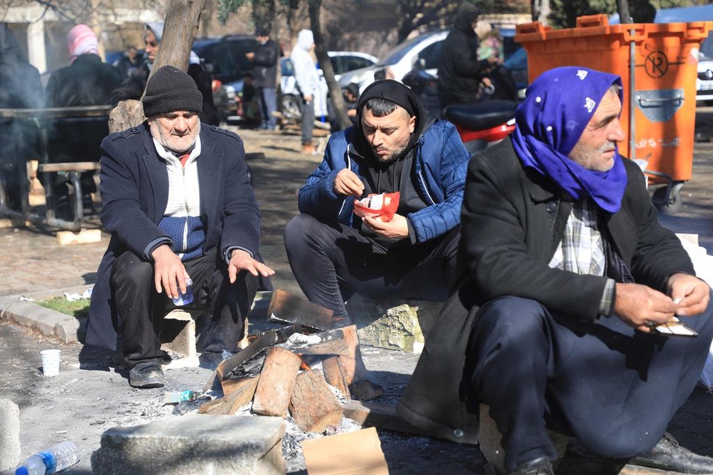 Warga makan dan menghangatkan badan di dekat api di sebuah jalan di Gaziantep, dekat dengan episentrum gempa, Turki tenggara, Selasa (7/2/2023). 