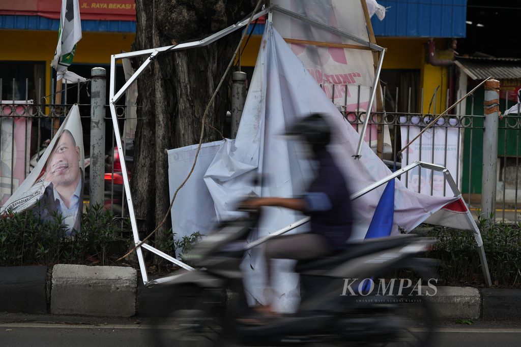 Pengendara sepeda motor melintasi baliho caleg yang sobek dan terlepas dari rangka baja ringan di Jalan Raya Bekasi, Jakarta Timur, Jumat (19/1/2024). 