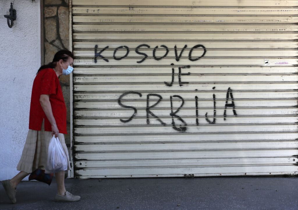 Seorang perempuan berjalan melewati grafiti yang berarti ”Kosovo adalah Serbia” di Belgrade, Serbia, Rabu (9/9/2020). Kosovo secara sepihak mendeklarasikan kemerdekaannya dari Serbia pada 2008 setelah sekitar satu dekade Belgrade mengirim pasukan untuk mengatasi kelompok separatis beretnis Albania. Serbia menolak mengakui negara Kosovo dan sejak saat itu ketegangan terus berlangsung. (AP Photo/Darko Vojinovic)