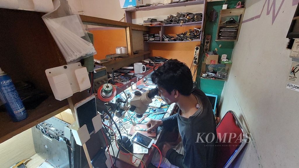 Haidi (37) memperbaiki telepon seluler milik pelanggan di tempat usaha jasa servis ponsel dan laptop yang dikelolanya di Kota Banjarmasin, Kalimantan Selatan, Selasa (6/9/2022). Sebagai pekerja informal, Haidi termasuk dalam generasi <i>sandwich</i>.