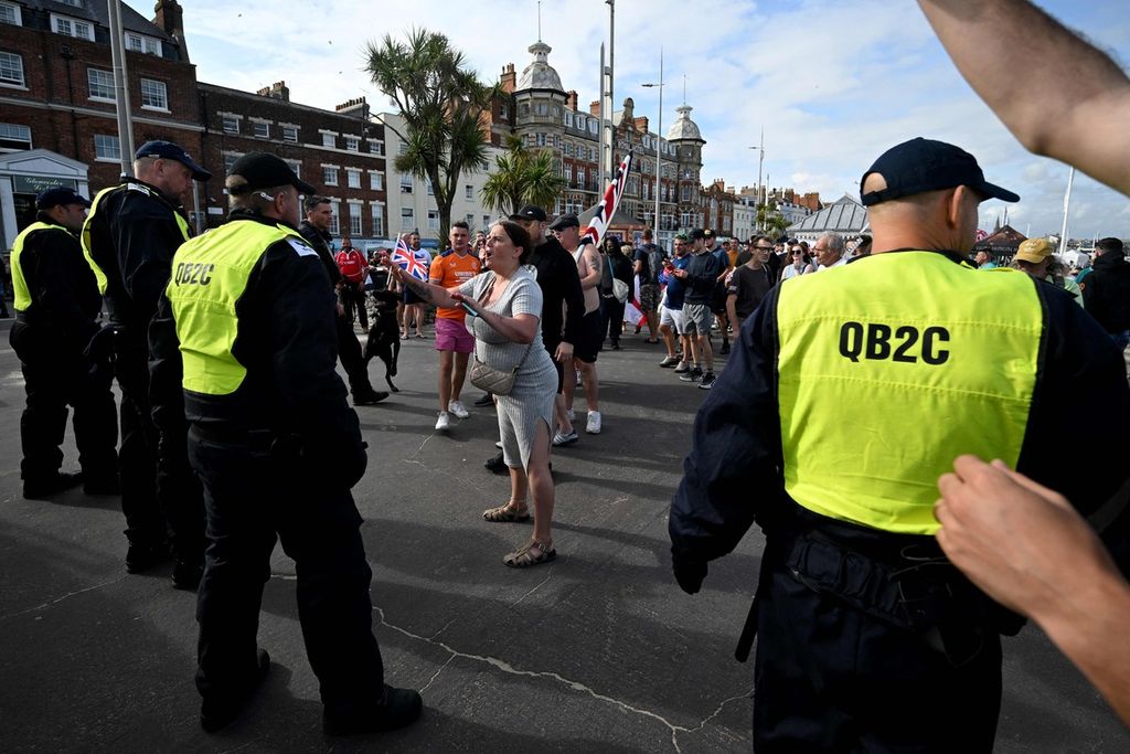  Pengunjuk rasa berteriak di depan polisi dalam aksi demonstrasi yang dilakukan para pendukung sayap kanan di Weymouth, di barat daya Inggris, MInggu (4/8/2024). 