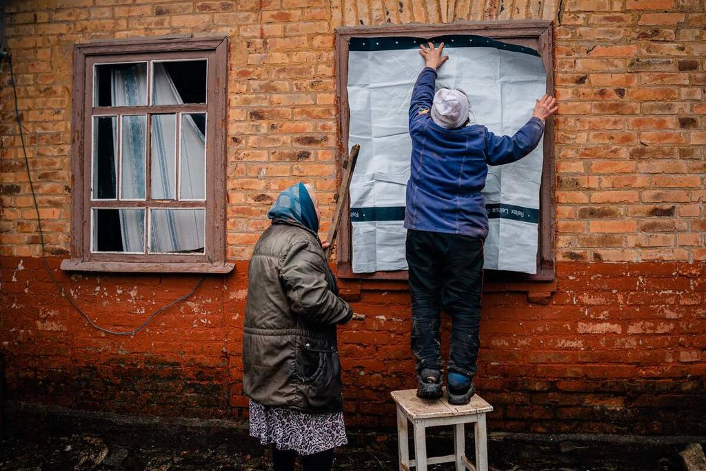 Dua warga senior Ukraina tengah menutup jendela rumah mereka dengan lembaran plastik, Selasa (28/2/2023). Rumah yang berada di Chasiv Yar, tak jauh dari Bakhmut rusak akiibat dalam serangan artileri Rusia. 