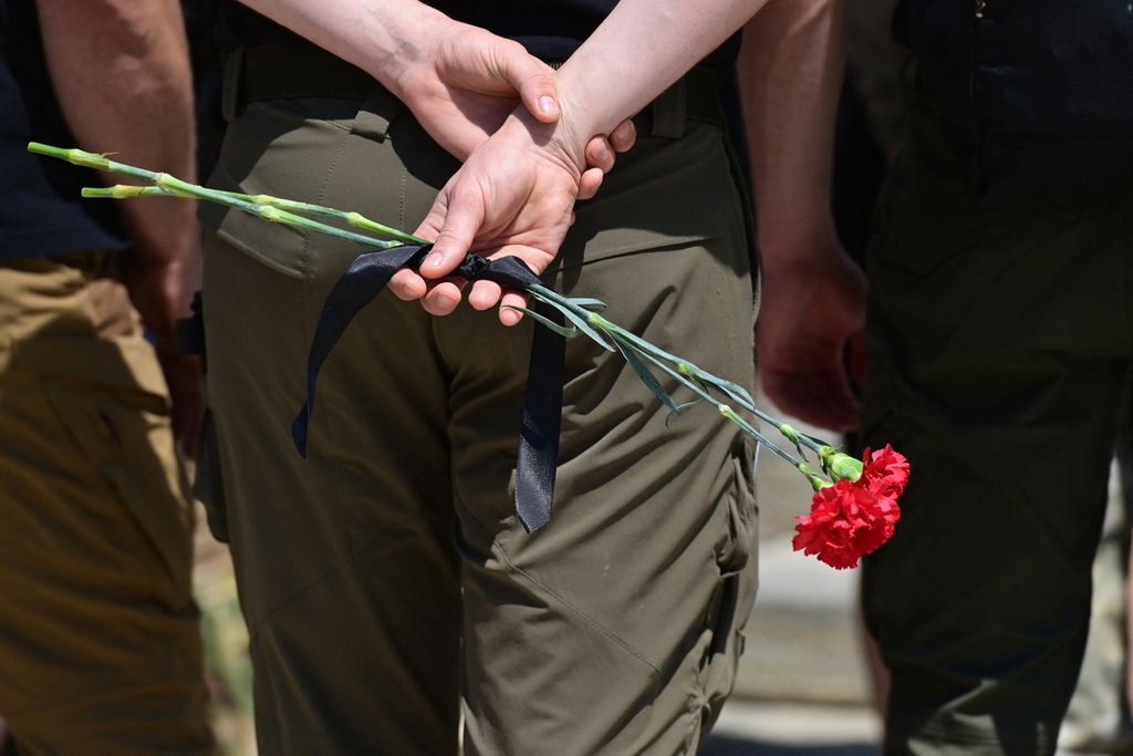 Seorang tentara memegang bunga <i>carnation</i> merah saat menghadiri pemakaman seorang prajurit Ukraina di Biara St Michael, Kyiv, Ukraina, 30 Juni 2022. 