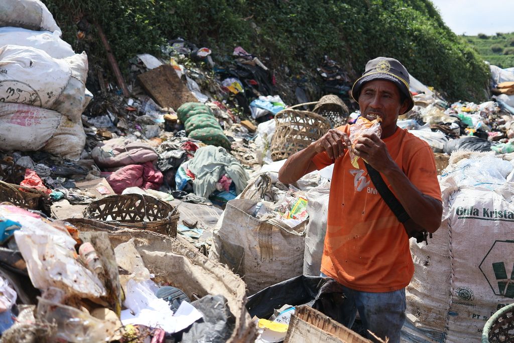 Rohadi (47) sedang menyantap roti sobek yang ia temukan ketika mengais sampah di TPA Bantar Gebang, Bekasi pada Selasa (26/4/2022).
