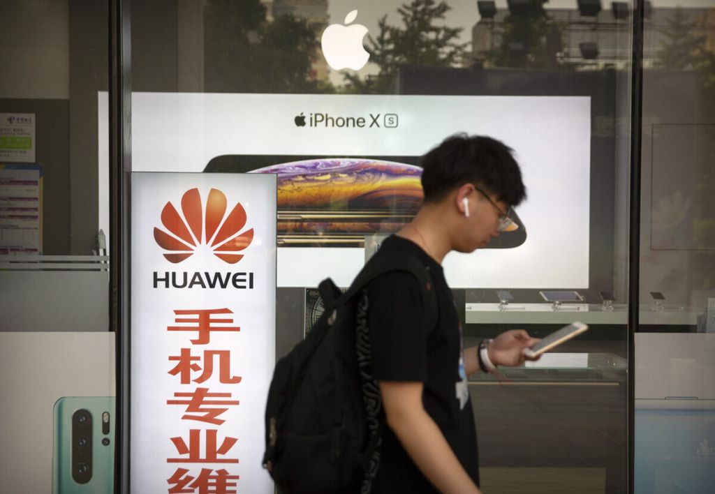Seorang pria berjalan melewati papan iklan telepon Huawei dan Apple di Beijing, China, 24 Mei 2019. 