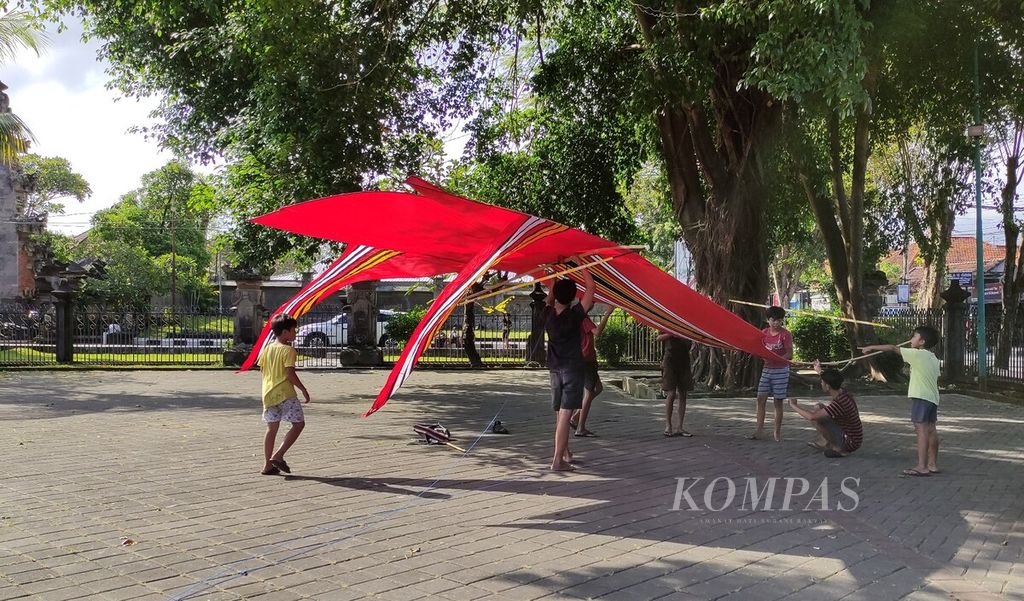 Sekelompok pemuda dan remaja putra menurunkan layang-layang <i>bebean</i> di area parkir Taman Werdhi Budaya Bali, Kota Denpasar, Sabtu (27/5/2023). Aktivitas <i>melayangan</i>, atau bermain layang-layang, tidak hanya sebatas hiburan, tetapi juga upaya merawat tradisi dan kepedulian terhadap lingkungan. 