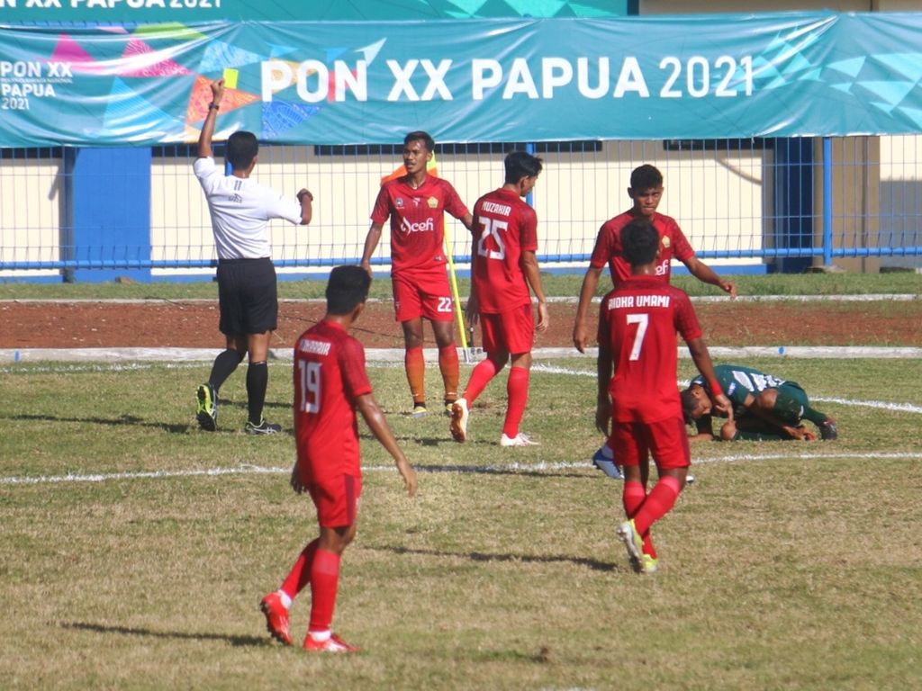 Wasit Thoriq Alkatiri (putih) memberikan kartu kuning kepada bek Aceh, Yasvani, pada laga semifinal PON 2021 antara Aceh kontra Jawa Timur, Selasa (12/10/2021), di Stadion Barnabas Youwe. Aceh menang, 2-1, dan melaju ke babak final untuk menghadapi Papua.