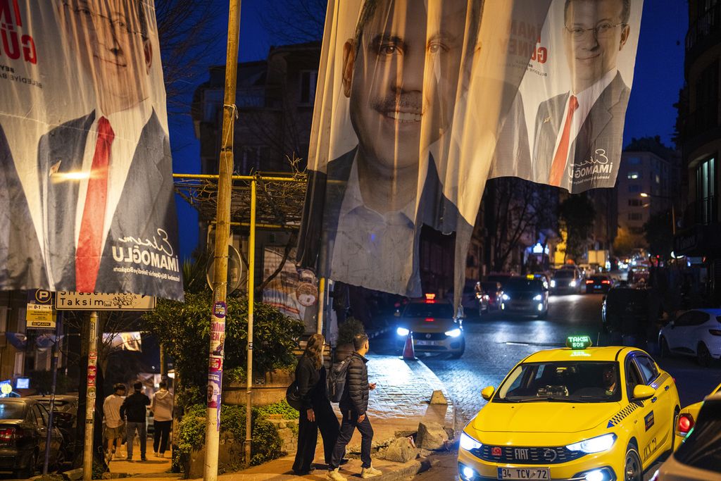 Warga berjalan di bawah <i>banner</i> bergambar kandidat wali kota Istanbul, yakni Murat Kurum (tengah), kandidat Partai Keadilan dan Pembangunan (AKP); serta Ekrem Imamoglu, wali kota petahana dan kandidat Partai Rakyat Republik (CHP), di Istanbul, Turki, 29 Maret 2024. 