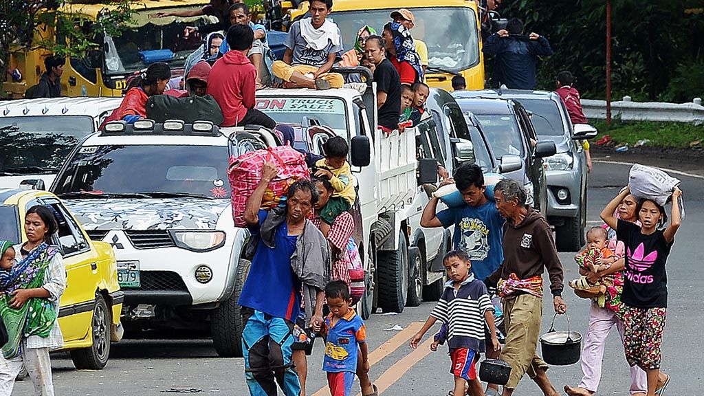 Satu keluarga membawa barang-barang milik mereka berjalan kaki mendahului antrean kendaraan pengungsi yang meninggalkan Marawi, Pulau Mindanao, Filipina, Jumat (26/5), di tengah pertempuran yang berkecamuk antara pasukan pemerintah dan milisi dari kelompok militan Maute yang menguasai kota itu. Sehari sebelumnya, pasukan pemerintah mengatakan telah mengebom kawasan perumahan tempat kelompok militan berlindung dan menyandera warga sipil. 