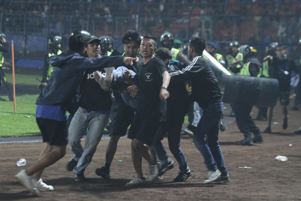 Sejumlah penonton membawa rekannya yang pingsan akibat sesak nafas terkena gas air mata yang ditembakkan aparat keamanan saat kericuhan usai pertandingan sepak bola BRI Liga 1 antara Arema melawan Persebaya di Stadion Kanjuruhan, Malang, Sabtu (1/10/2022).