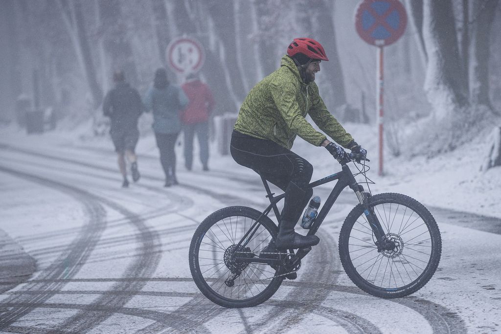 Seorang pengendara sepeda dan pelari melintas di jalan saat salju pertama turun tahun ini di Het Drielandenpunt, Vaals, Belanda, 7 Januari 2021. 