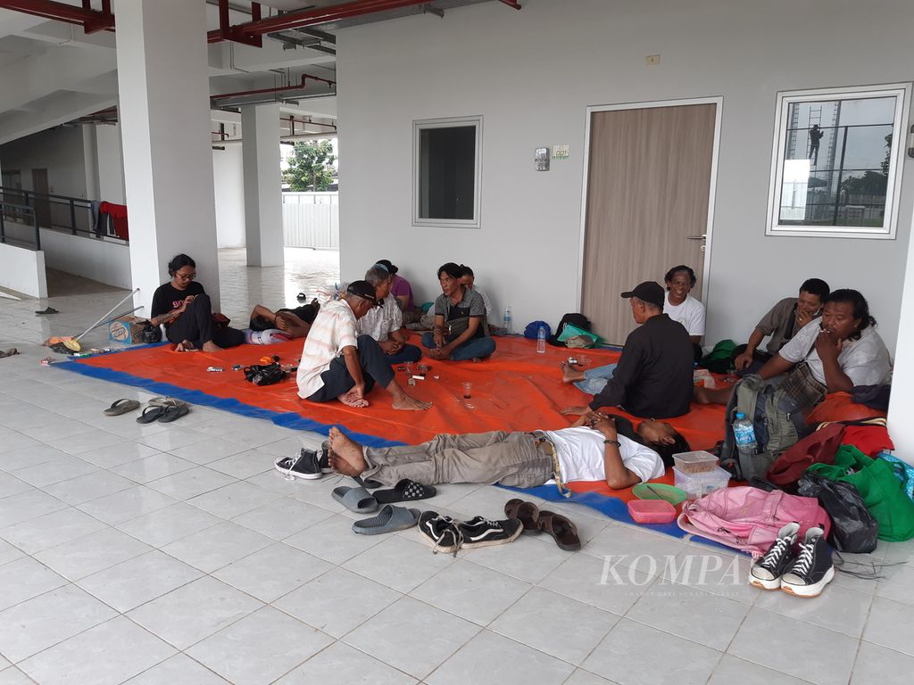 Warga yang dijanjikan untuk menghuni Kampung Susun Bayam duduk mengobrol hingga berbaring di pelataran Kampung Susun Bayam, Jakarta Utara, Selasa (14/3/2023) sore. Mereka merupakan warga yang direlokasi tiga tahun lalu untuk pembangunan Jakarta International Stadium.