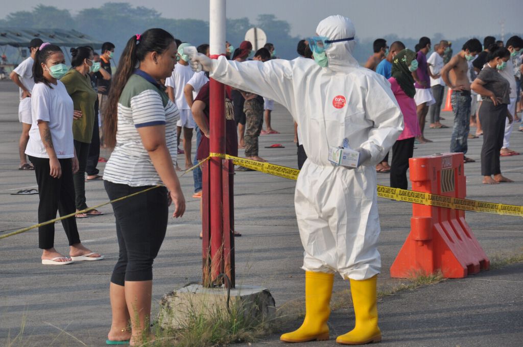 An officer wearing protective gear checks the temperature of an Indonesian migrant worker who arrived from Malaysia during quarantine to prevent the spread of coronavirus disease (COVID-19), before getting exercise at Soewondo air base in Medan, North Sumatra province, Indonesia, April 11, 2020. 