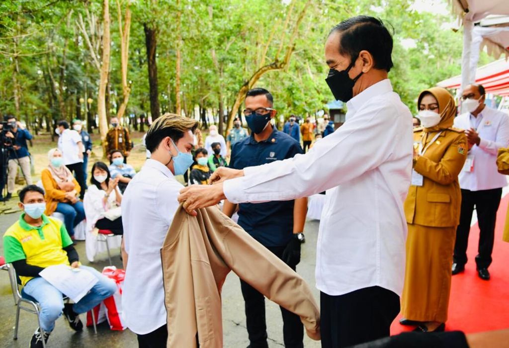 Presiden Jokowi memberikan jaketnya kepada peserta vaksinasi ketika meninjau pelaksanaan vaksinasi Covid-19 massal yang digelar di halaman Kantor Gubernur Sulawesi Tenggara, Kota Kendari, pada Rabu (30/6/2021). 