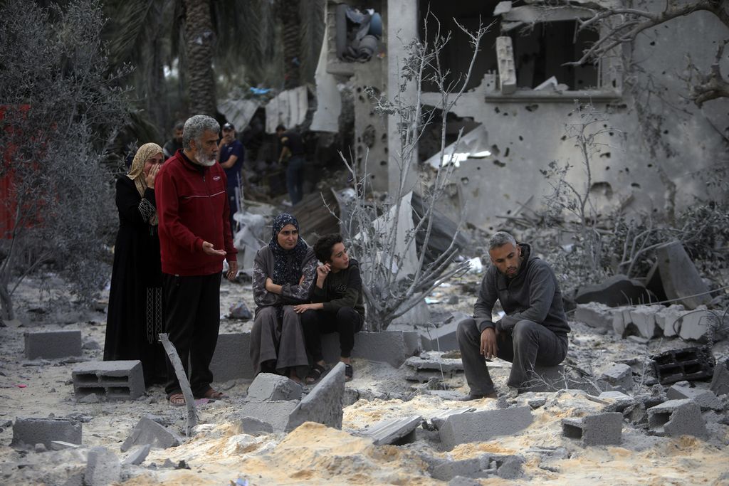 Beberapa orang warga Palestina duduk di atas puing-puing rumah yang hancur akibat serangan udara militer Israel di kota Khan Younis, Jalur Gaza, Rabu (22/11/2023). 