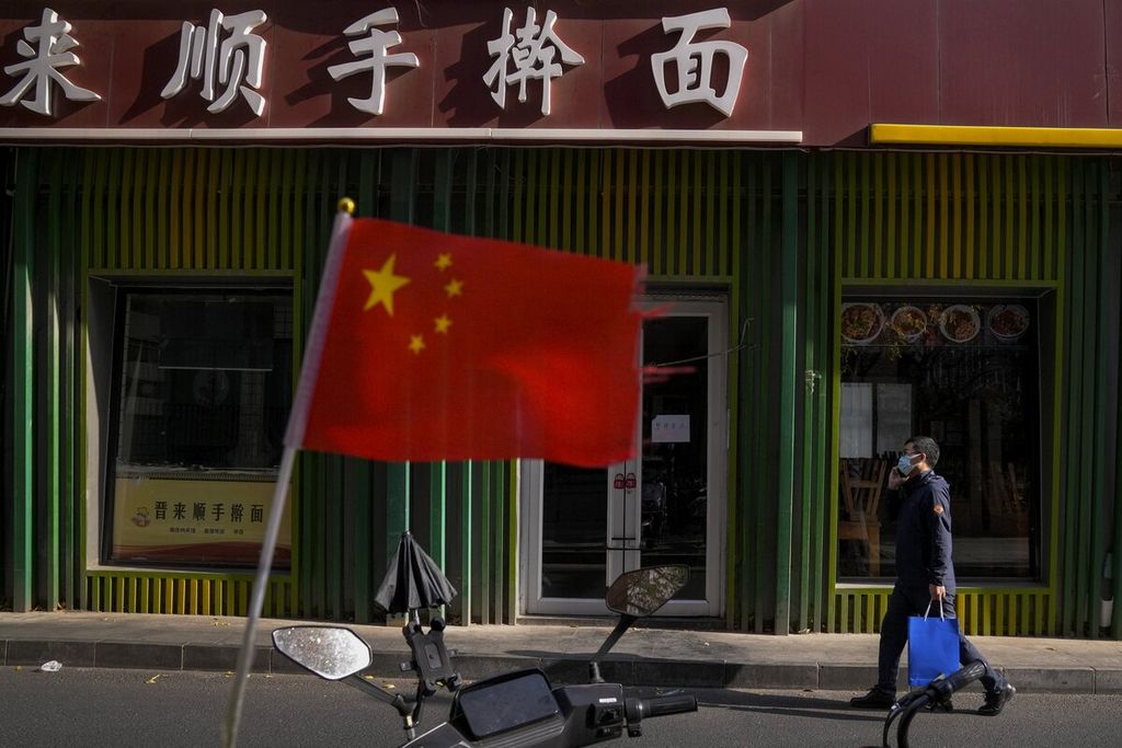 Seorang pria mengenakan masker saat berjalan melewati bendera China di luar restoran mi yang tutup akibat kebijakan ketat Covid-19 di Beijing, China, 23 November 2022.