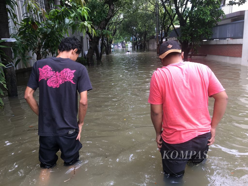 Eko (kanan) dan Ade (kiri) menerjang banjir di Jalan Wana Mulya Utama, Karang Mulya, Karang Tengah, Kota Tangerang, Banten, demi datang ke TPS pada Rabu (14/2/2024) siang.
