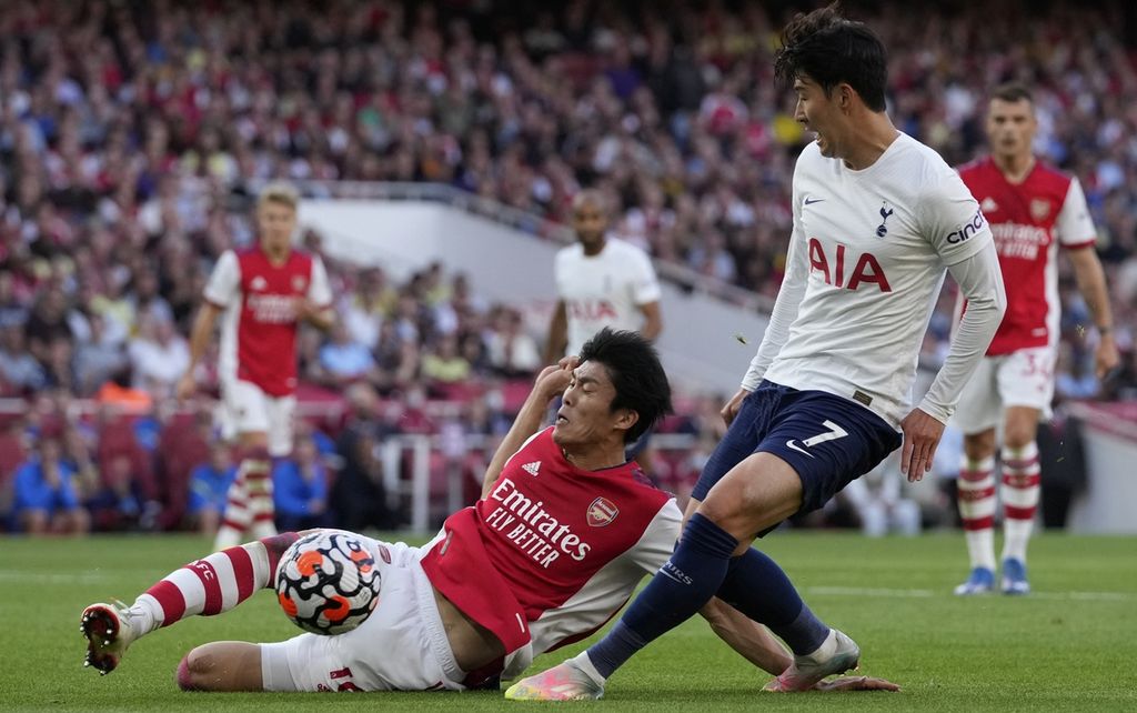 Bek Arsenal, Takehiro Tomiyasu (kiri), menghalau bola yang berusaha dikuasai penyerang Tottenham Hotspur, Son Heung-min, dalam laga pekan keenam Liga Inggris di Stadion Emirates, London, Inggris, Senin (27/9/2021) dini hari. 